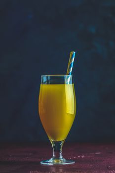 Glass of pineapple tropical fresh juice on dark bordo concrete surface table. Summer drinks and alcoholic cocktails.