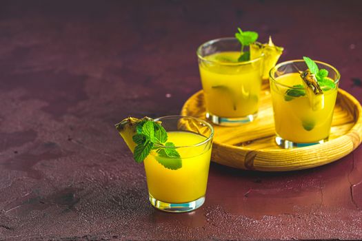 Cold cocktail with squeezed pineapple juice, lime and mint in glasses on concrete surface table. Summer drinks and alcoholic cocktails.
