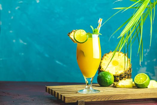 Cold cocktail with squeezed pineapple juice, lime and mint in tall glass on concrete surface table. Summer drinks and alcoholic cocktails.