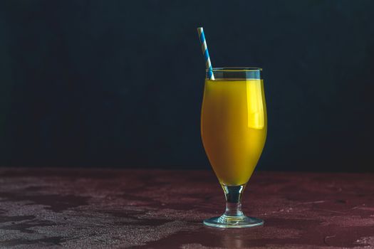 Glass of pineapple tropical fresh juice on dark bordo concrete surface table. Summer drinks and alcoholic cocktails.