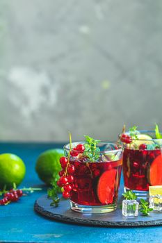 Cold red cocktail with currant, lime, mint, thyme and ice in glass on dark concrete surface table. Summer drinks and alcoholic cocktails. Alcoholic cocktail Currant mojito.