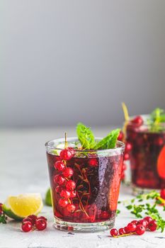 Cold red cocktail with currant, lime, mint, thyme and ice in glass on light gray concrete surface table. Summer drinks and alcoholic cocktails. Alcoholic cocktail Currant mojito.