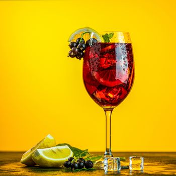 Cold red cocktail with blackcurrant, lemon, mint and ice in tall glass on yellow background. Summer drinks and alcoholic cocktails. Alcoholic cocktail Blackcurrant mojito