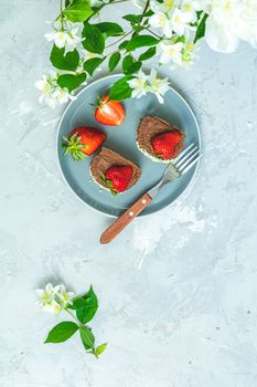 Chocolate rollcake with fresh strawberries on ceramic plate, jasmine and white peonies on light gray concrete surface table. Top view, flat lay, copy space for you text