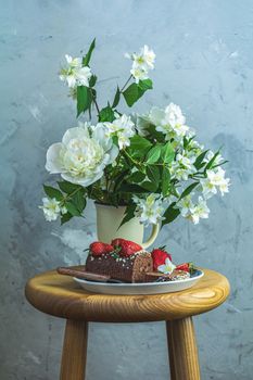 Chocolate roll cake with fresh strawberries, jasmine and white peonies in cup on wooden table. Artistic Still Life in the style of Dutch painting. Copy space for you text..