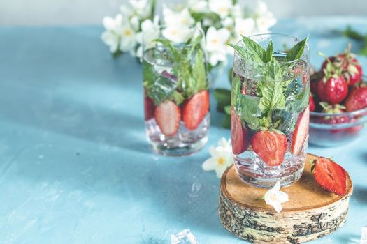 Detox infused water with strawberry and mint in highball glasses on blue concrete table background, copy space. Cold summer drink, mineral water.