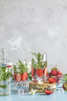 Detox infused water with strawberry and mint in highball glasses on blue concrete table background, copy space. Cold summer drink, mineral water.