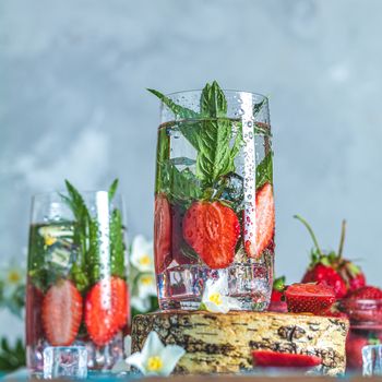 Detox infused water with strawberry and mint in highball glasses on blue concrete table background, copy space. Cold summer drink. Mineral water.