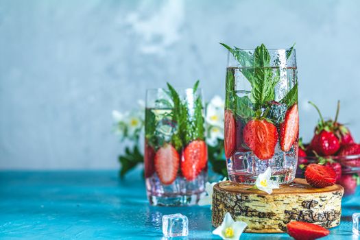 Detox infused water with strawberry and mint in highball glasses on blue concrete table background, copy space. Cold summer drink. Mineral water.