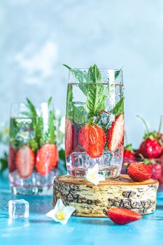Detox infused water with strawberry and mint in highball glasses on blue concrete table background, copy space. Cold summer drink. Mineral water.