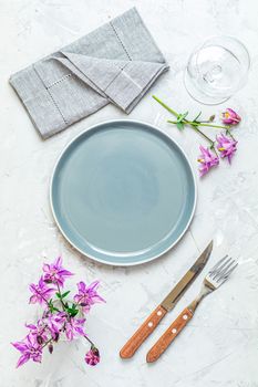Empty gray plate, cutlery, napkin and fresh pink bells granny's bonnet. Flat lay, top view