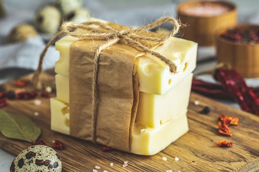 Pieces of cheese in paper on wooden board on the light gray concrete table surface. Copy space for you text.