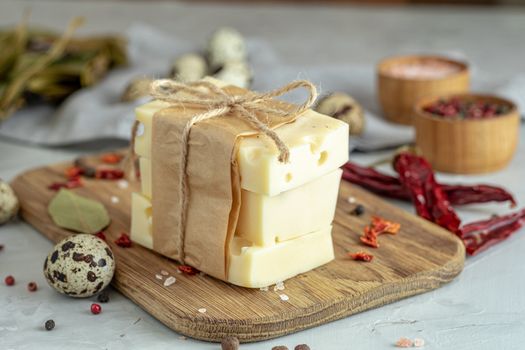 Pieces of cheese in paper on wooden board on the light gray concrete table surface. Copy space for you text.