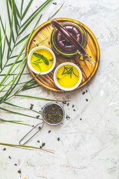 Asian tea set composition. Healthy life and relaxation concept. Glass tea pot, ceramic pot and green tea in strainer on light gray concrete table background. Top view, copy space for you text