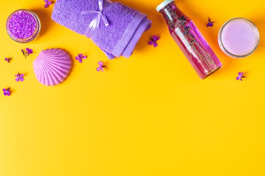 Spa products. Lavender bath salts, viola flowers, soap, cosmetic cream and towel. Violet purple concept. Flat lay on yellow background, top view.