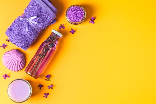 Spa products. Lavender bath salts, viola flowers, soap, cosmetic cream and towel. Violet purple concept. Flat lay on yellow background, top view.