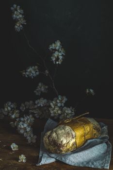 Freshly baked rye handmade breads on old wooden table with linen napkin and apricot tree blossom branch. Dark rustic style. Photo styling of paintings by Flemish painters