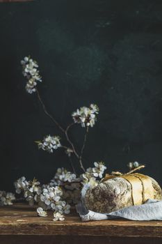 Freshly baked rye handmade breads on old wooden table with linen napkin and apricot tree blossom branch. Dark rustic style. Photo styling of paintings by Flemish painters