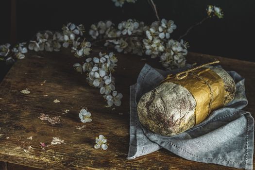 Freshly baked rye handmade breads on old wooden table with linen napkin and apricot tree blossom branch. Dark rustic style. Photo styling of paintings by Flemish painters