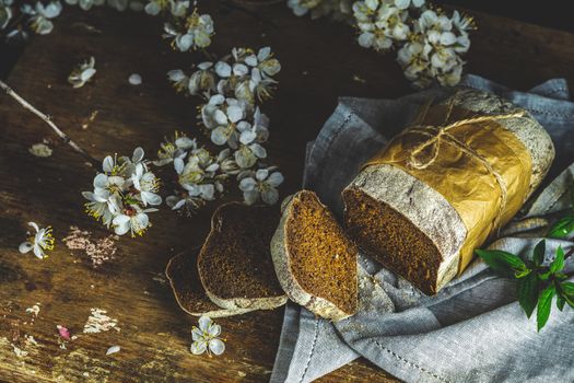 Sliced freshly baked rye handmade breads on old wooden table with linen napkin and apricot tree blossom branch. Dark rustic style.