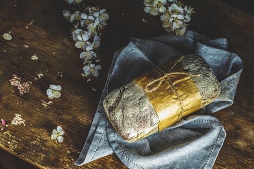 Freshly baked rye handmade breads on old wooden table with linen napkin and apricot tree blossom branch. Dark rustic style. Photo styling of paintings by Flemish painters
