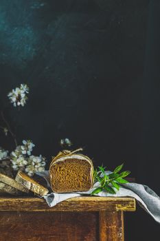 Sliced freshly baked rye handmade breads on old wooden table with linen napkin and apricot tree blossom branch. Dark rustic style.