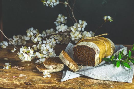 Sliced freshly baked rye handmade breads on old wooden table with linen napkin and apricot tree blossom branch. Dark rustic style.