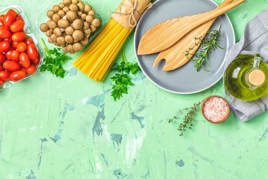 Spaghetti, shimeji mushroom, tomatoes, olive oil,  pink salt, empty ceramic bowl, wooden spoons for salad over green concrete texture background. Top view, healthy food concept, top view, copy space