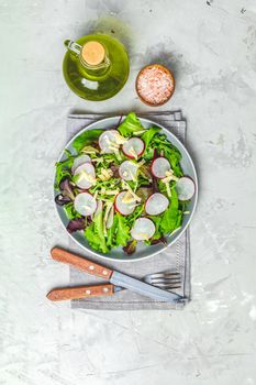Salad with radishes, olive oil, pink salt, knife and fork for salad over gray concrete texture background. Top view, healthy food concept, top view, copy space for you text.