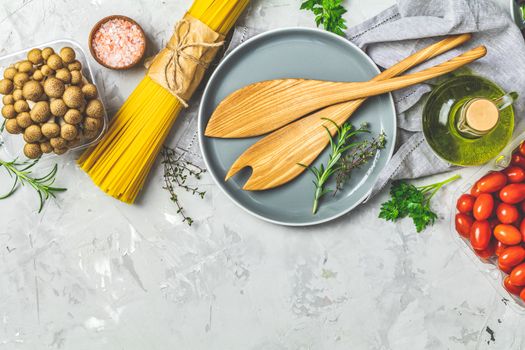 Spaghetti, shimeji mushroom, tomatoes, olive oil,  pink salt, empty ceramic bowl, wooden spoons for salad over gray concrete texture background. Top view, healthy food concept, top view, copy space