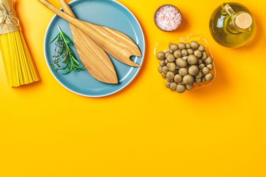 Spaghetti, shimeji mushroom, olive oil,  pink salt, empty ceramic bowl, wooden spoons for salad over yellow background. Top view, flat lay, healthy food concept, copy space for you text.
