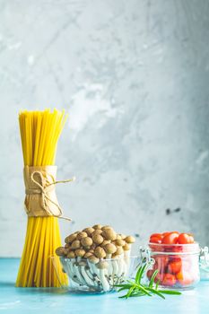Spaghetti, shimeji mushroom, olive oil,  pink salt, empty ceramic bowl, wooden spoons for salad over blue concrete background. Healthy food concept, copy space for you text.