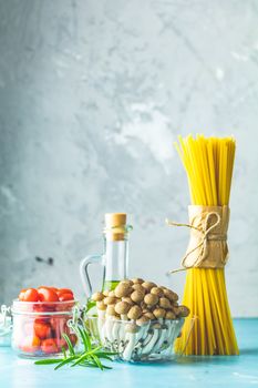 Spaghetti, shimeji mushroom, olive oil,  pink salt, empty ceramic bowl, wooden spoons for salad over blue concrete background. Healthy food concept, copy space for you text.