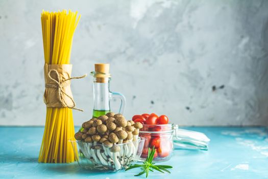 Spaghetti, shimeji mushroom, olive oil,  pink salt, empty ceramic bowl, wooden spoons for salad over blue concrete background. Healthy food concept, copy space for you text.