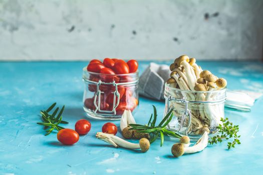 Buna Shimeji - edible mushroom from East Asia. Good food for good health. Clump of shimeji mushroom and cherry tomatoes in jars on blue concrete surface background