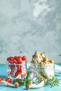 Buna Shimeji - edible mushroom from East Asia. Good food for good health. Clump of shimeji mushroom and cherry tomatoes in jars on blue concrete surface background