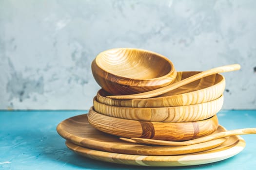 Variety of wooden bowl, wooden spoons for salad over blue texture background. Food or ecology kitchen concept. Copy space for you text.