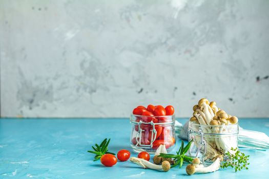 Buna Shimeji - edible mushroom from East Asia. Good food for good health. Clump of shimeji mushroom and cherry tomatoes in jars on blue concrete surface background