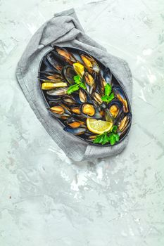 Seafood mussels with lemon and parsley in black metal plate on light gray concrete table surface, top view, copy space for you text
