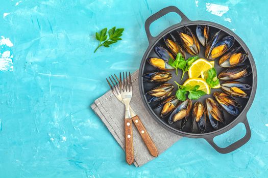 Seafood mussels with lemon and parsley in black metal pan on blue concrete table surface, top view, copy space for you text