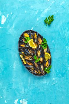 Seafood mussels with lemon and parsley in black metal plate on blue concrete table surface, top view, copy space for you text