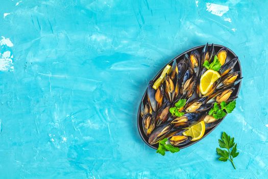 Seafood mussels with lemon and parsley in black metal plate on blue concrete table surface, top view, copy space for you text