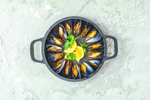 Seafood mussels with lemon and parsley in black metal pan on light gray concrete table surface, top view, copy space for you text