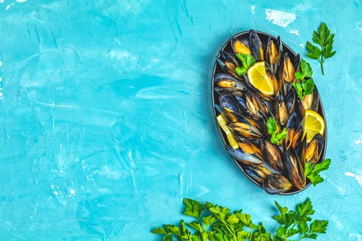 Seafood mussels with lemon and parsley in black metal plate on blue concrete table surface, top view, copy space for you text