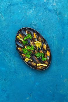 Seafood mussels with lemon and parsley in black metal plate on dark blue concrete table surface, top view, copy space for you text