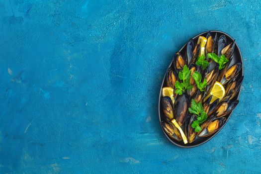 Seafood mussels with lemon and parsley in black metal plate on dark blue concrete table surface, top view, copy space for you text