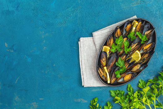 Seafood mussels with lemon and parsley in black metal plate on dark blue concrete table surface, top view, copy space for you text
