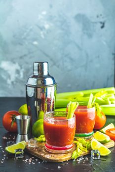 Tomato juice with celery, spices, salt and ice in portion glasses with copy space. Bloody Mary cocktail. Alcoholic drink and ingredients at dark concrete table surface