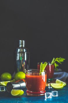 Tomato juice with celery, spices, salt and ice in portion drink glasses with copy space. Bloody Mary cocktail. Alcoholic drink and ingredients at dark blue concrete table surface.