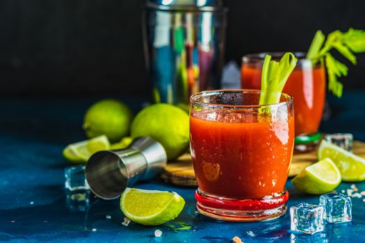Tomato juice with celery, spices, salt and ice in portion glasses with copy space. Bloody Mary cocktail. Alcoholic drink and ingredients at dark concrete table surface